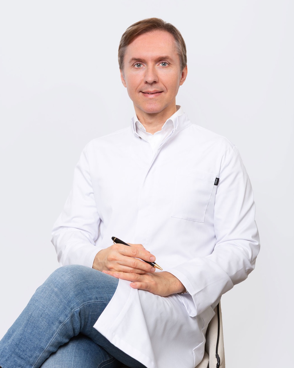 Dr. med. Denis Alekseev im weißen Arztkittel, sitzend mit Stift in der Hand